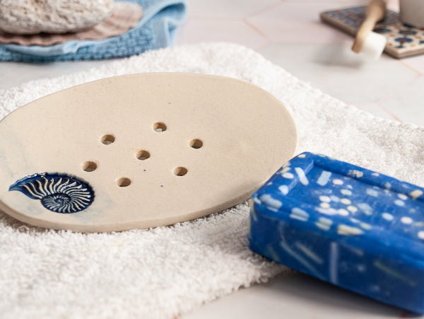 Blaue Mosaik-Seifenstück neben Seifenunterlage auf weißem Teppich, reich an Olivenöl, duftet nach Lilien und Freesien